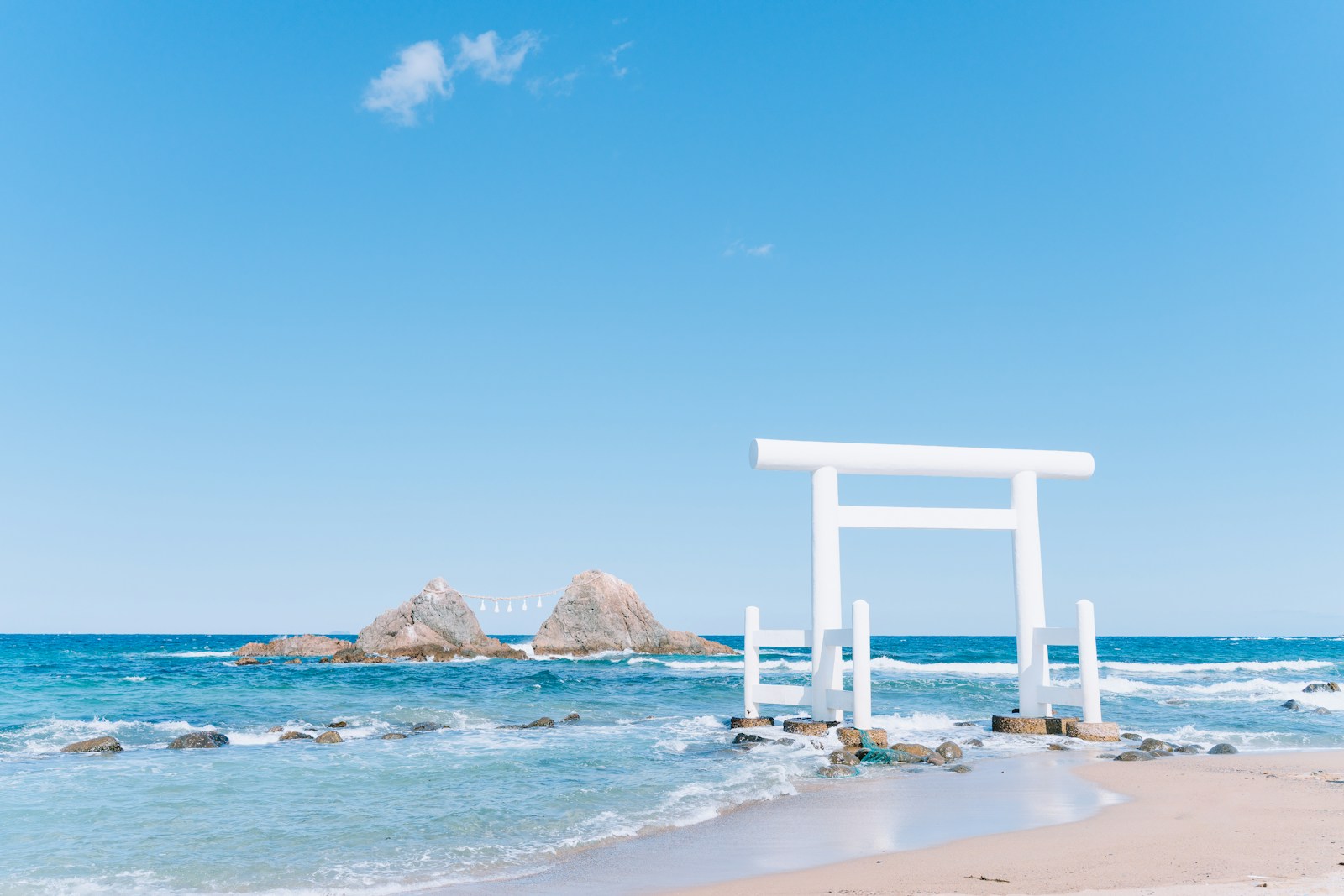 A white shrine gate stands in the blue ocean.